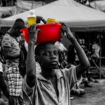 Boy in Sierra Leone with red bucket on his head while he works.